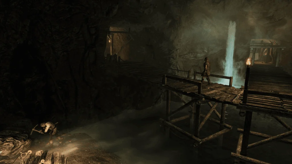 An Imperial guard walks across an elevated wooden catwalk in an underground mine while a worker below mines precious minerals by lantern light. A waterfall illuminates the background behind them.